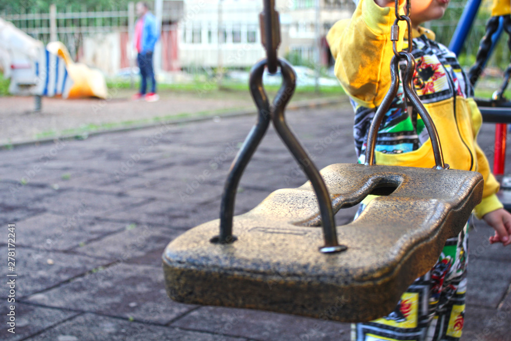 Children's swing close-up. The boy stands next to the swing on the Playground. The theme of safety in playgrounds. What to do for a walk with a child. The child and the swing.