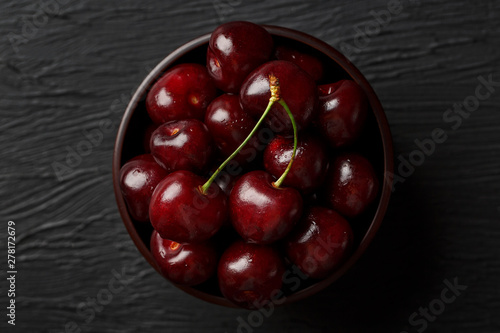 Ripe and juicy cherry berries on a black textural background in a brown cup, with water drops. Top view, close-up.