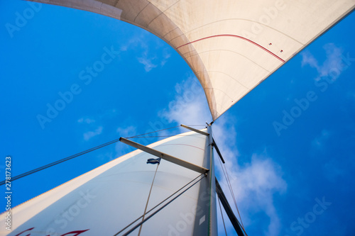 Top of yacht: mast and sail filled by the wind. The wind has filled the spinnaker on sailing yacht. Bottom view. Mast and sail against blue sky and white clouds. Yachting Ship Equipment. Diagonal shot