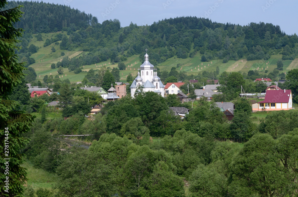 View of the Carpathian village: catholic church, country houses, gardens and mountains.  Lugi village, Ukraine