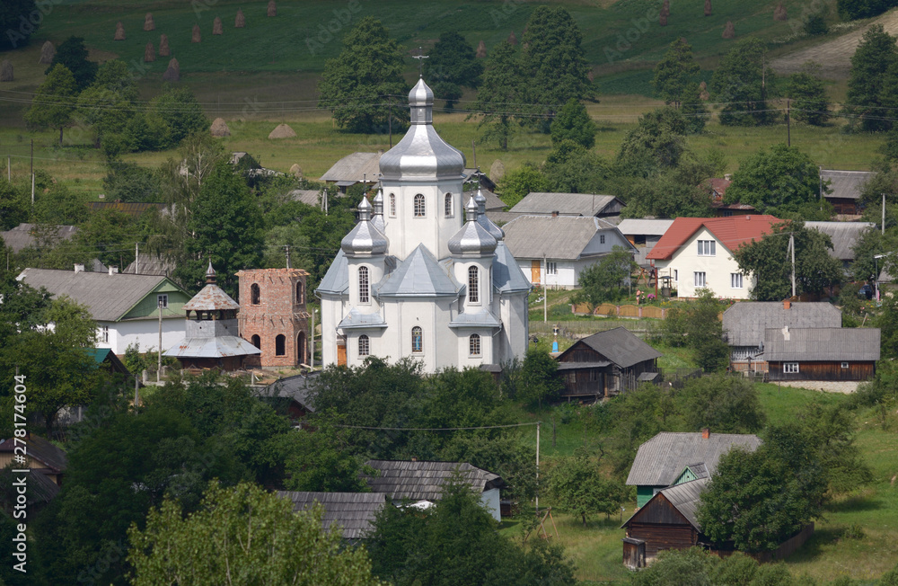 View of the Carpathian village: catholic church, country houses, gardens and mountains. Lugi village, Ukraine
