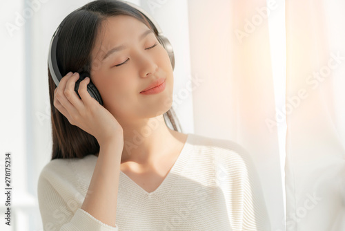 relex and peaceful asian woman enjoy weekend with music headphone morning sunlight near window home background photo