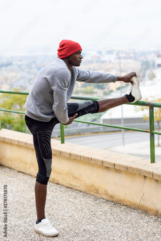 Black man doing stretching before running in urban background