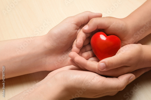 Woman and child holding heart on beige wooden background  closeup. Donation concept