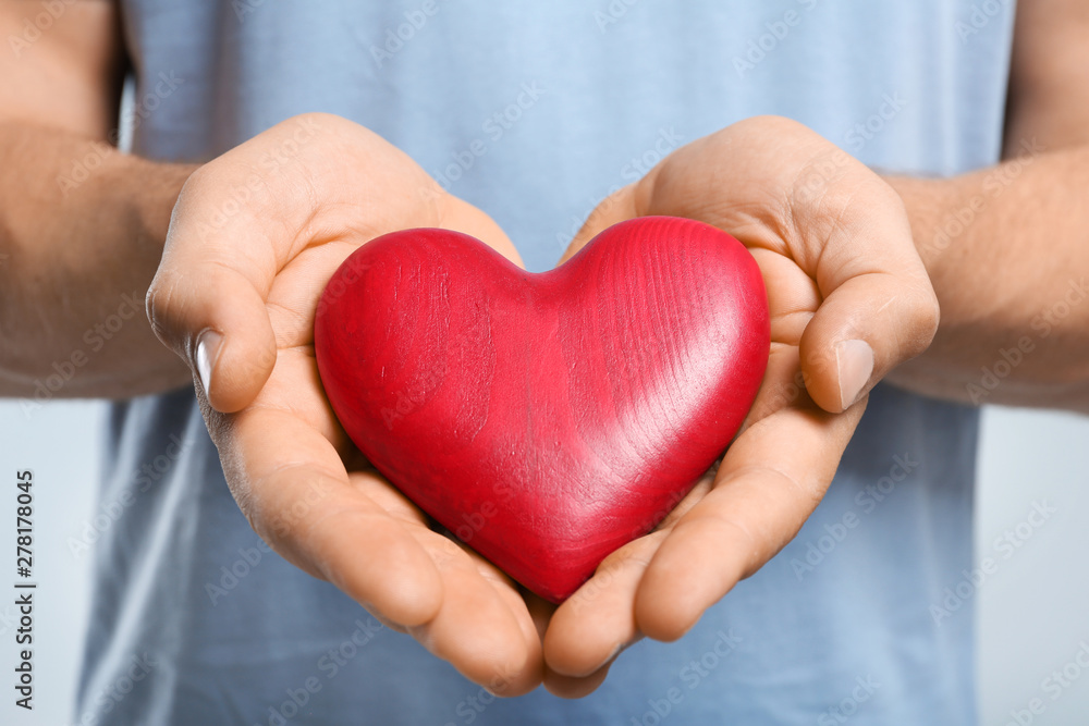 Young man holding red heart on color background, closeup. Donation concept