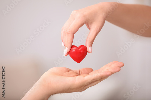 Woman giving red heart to man on blurred background, closeup. Donation concept