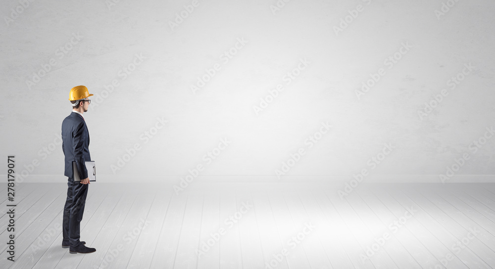 Young architect with construction helmet standing in an empty space and holding a plan Young architect with construction helmet standing in an empty space and holding a plan