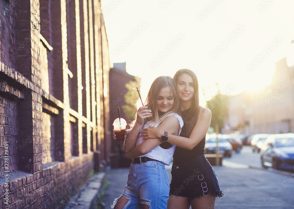 Two beautiful girls with drinks laughing in sunset