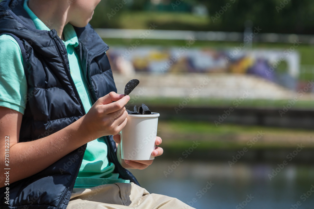 Black chips. Black potato chips in the hands of a teenager on the background of a sunny summer landscape. Black chips. Black potato chips in the hands of a teenager on the background of a sunny summer landscape.