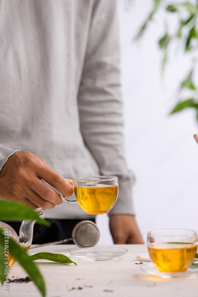Male hands holding cup of tea glass on light background Male hands holding cup of tea glass on light background