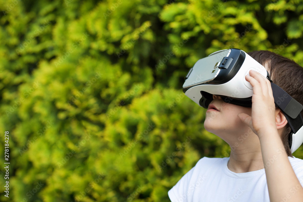 Cute little boy using VR glasses outdoors in a park - Blogger testing augmented reality goggles concept - Gamer exulting during 3D video game playing Cute little boy using VR glasses outdoors in a park - Blogger testing augmented reality goggles concept - Gamer exulting during 3D video game playing