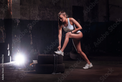 Attractive fit woman athlete tying shoelaces on tires, fit woman exercising with big tire.