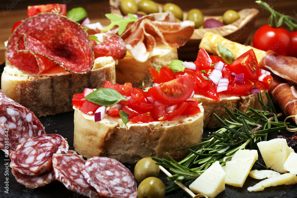 Traditional italian antipasto bruschetta appetizer with cherry tomatoes, cream cheese, basil leaves and balsamic vinegar on cutting board with prosciutto, salami, cheese Traditional italian antipasto bruschetta appetizer with cherry tomatoes, cream cheese, basil leaves and balsamic vinegar on cutting board with prosciutto, salami, cheese
