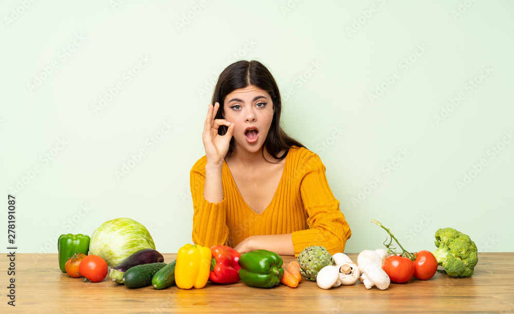 Teenager girl with many vegetables surprised and showing ok sign