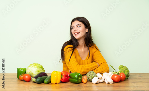 Teenager girl with many vegetables with arms crossed and happy