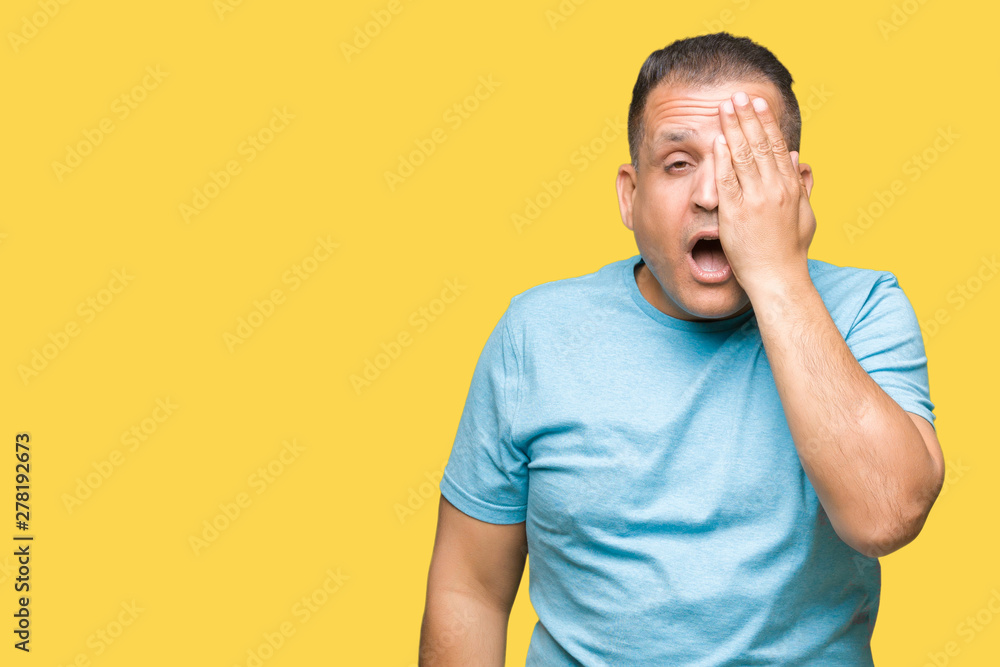 Middle age arab man wearing blue t-shirt over isolated background covering one eye with hand with confident smile on face and surprise emotion. Middle age arab man wearing blue t-shirt over isolated background covering one eye with hand with confident smile on face and surprise emotion.