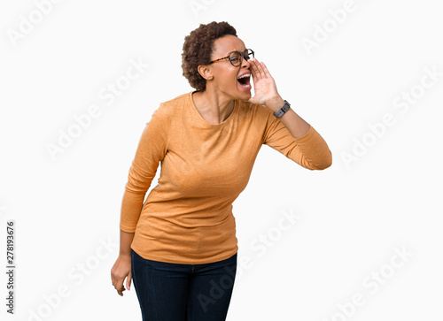 Young beautiful african american woman wearing glasses over isolated background shouting and screaming loud to side with hand on mouth. Communication concept. © Krakenimages.com