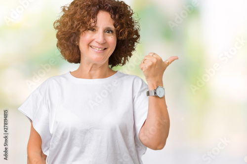 Beautiful middle ager senior woman wearing white t-shirt over isolated background smiling with happy face looking and pointing to the side with thumb up.