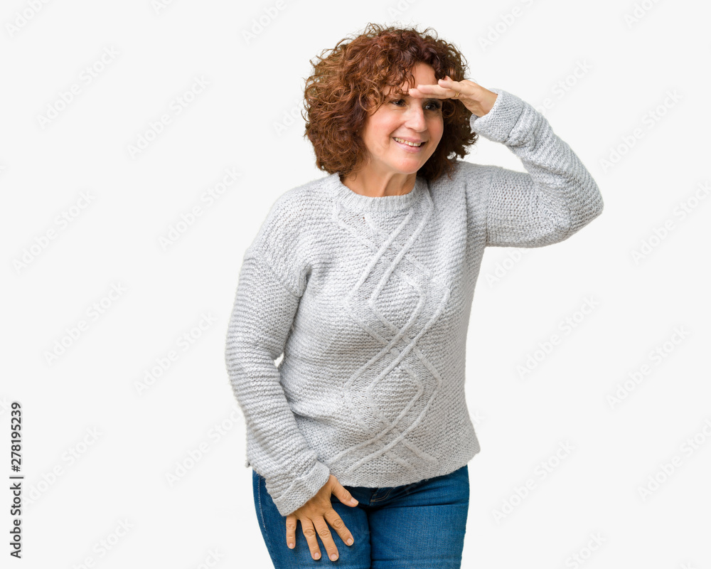 Beautiful middle ager senior woman wearing winter sweater over isolated background very happy and smiling looking far away with hand over head. Searching concept. Beautiful middle ager senior woman wearing winter sweater over isolated background very happy and smiling looking far away with hand over head. Searching concept.