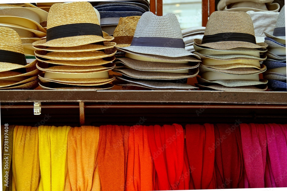 several straw hats and colorful scarves for sale at an outdoor market in Verona, Italy. Group of colored hats showcase perspective market shop. Colors of textiles.