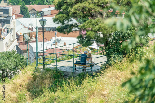 Rear view of a man and a woman on a bench on a sunny day under a tree. Contemplative and desirable mood.