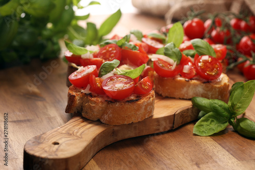 Traditional italian antipasto bruschetta appetizer with cherry tomatoes, cream cheese, basil leaves and balsamic vinegar on cutting board. Antipasti