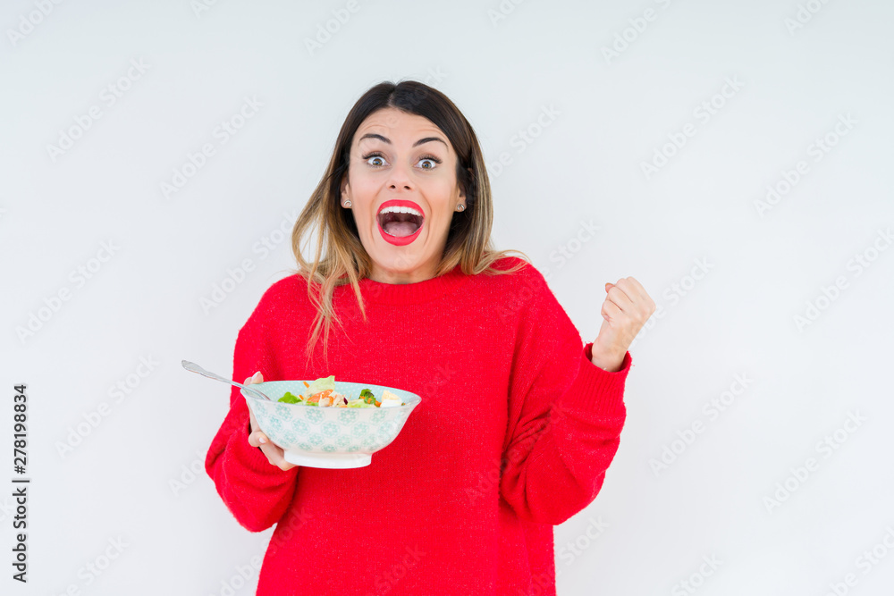 Young woman eating fresh healthy salad over isolated background very happy and excited, winner expression celebrating victory screaming with big smile and raised hands Young woman eating fresh healthy salad over isolated background very happy and excited, winner expression celebrating victory screaming with big smile and raised hands