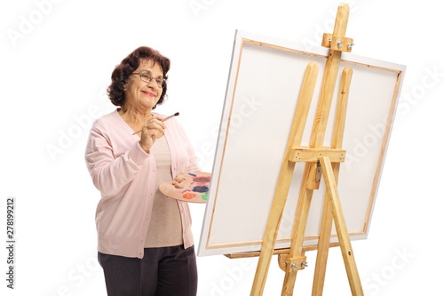 Happy elderly woman with a brush and paints painting on a canvas