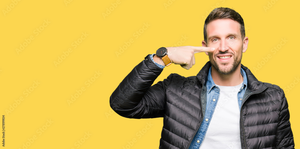 Naklejka premium Handsome man wearing winter coat Pointing with hand finger to face and nose, smiling cheerful