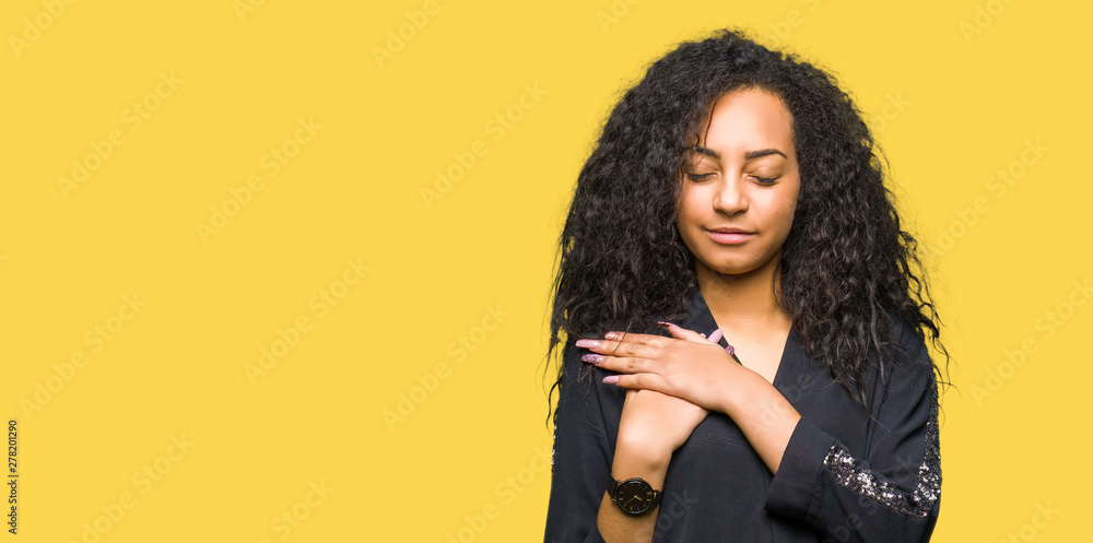 Young beautiful girl with curly hair wearing elegant dress smiling with hands on chest with closed eyes and grateful gesture on face. Health concept. Young beautiful girl with curly hair wearing elegant dress smiling with hands on chest with closed eyes and grateful gesture on face. Health concept.