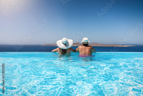Paar mit Sonnenhüten genießt den Sommerurlaub in einem infinity Pool mit Aussicht auf das Meer