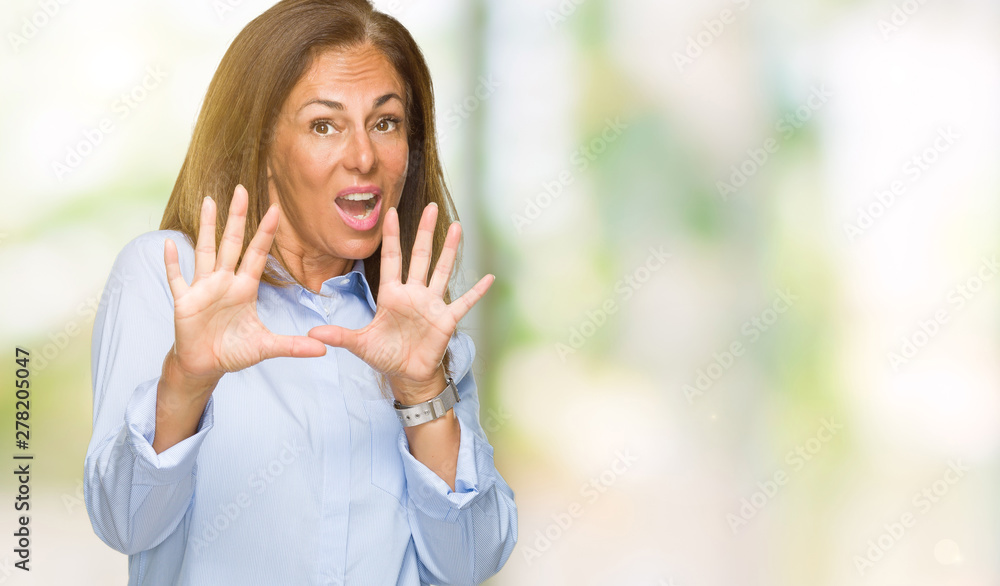 Beautiful middle age business adult woman over isolated background afraid and terrified with fear expression stop gesture with hands, shouting in shock. Panic concept.