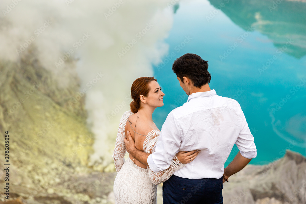 Bride and groom hugging against the backdrop of a green lake and volcanic smoke in the volcano crater