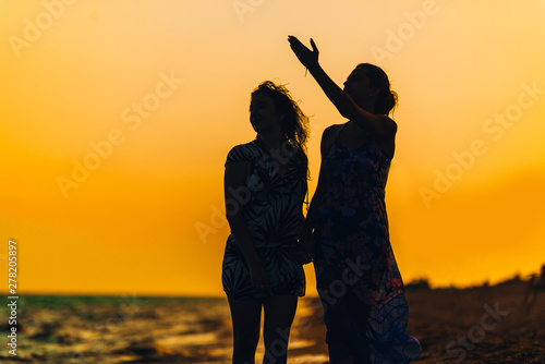 Silhouette of the girls standing at the beach during beautiful sunset