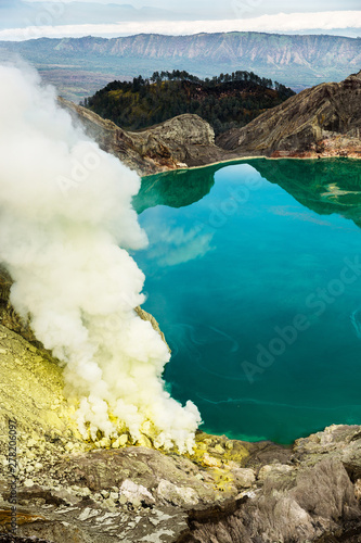 Crater of a volcano with a green sulfuric volcanic lake and volcanic smoke. View of the smoking volcano Kawah Ijen in Indonesia. Mountain landscape