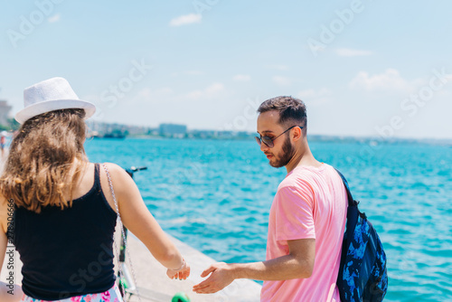 Cute couple walking by the sea on a boardwalk while the girl holds a palette and smiles to her boyfriend.