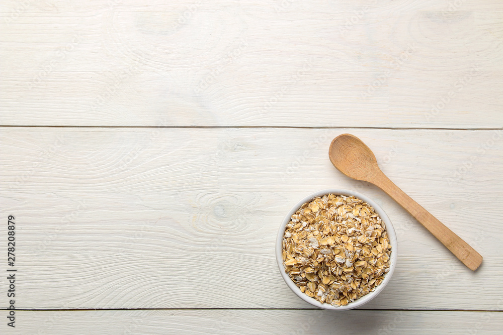 Dry oatmeal flakes in a bowl and spoon on a white wooden table. healthy nutrition. healthy food. top view Dry oatmeal flakes in a bowl and spoon on a white wooden table. healthy nutrition. healthy food. top view