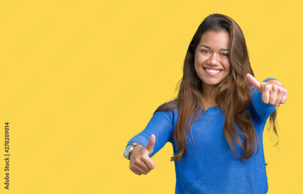 Young beautiful brunette woman wearing blue sweater over isolated background approving doing positive gesture with hand, thumbs up smiling and happy for success. Looking at the camera, winner gesture. Young beautiful brunette woman wearing blue sweater over isolated background approving doing positive gesture with hand, thumbs up smiling and happy for success. Looking at the camera, winner gesture.
