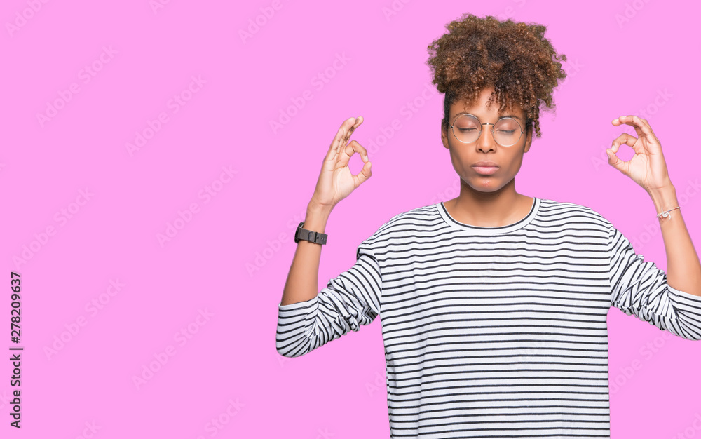 Beautiful young african american woman wearing glasses over isolated background relax and smiling with eyes closed doing meditation gesture with fingers. Yoga concept. Beautiful young african american woman wearing glasses over isolated background relax and smiling with eyes closed doing meditation gesture with fingers. Yoga concept.