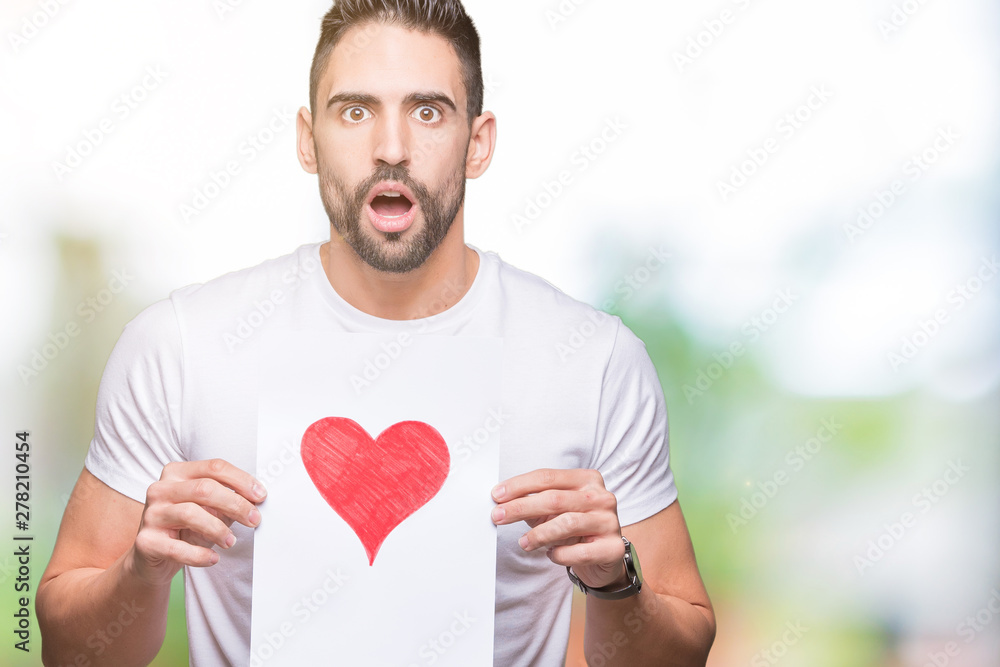 Handsome young man holding card with red heart over isolated background scared in shock with a surprise face, afraid and excited with fear expression Handsome young man holding card with red heart over isolated background scared in shock with a surprise face, afraid and excited with fear expression