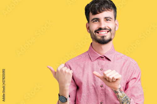 Young handsome man wearing pink shirt over isolated background Pointing to the back behind with hand and thumbs up, smiling confident photo