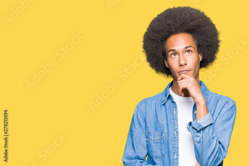 Young african american man with afro hair with hand on chin thinking about question, pensive expression. Smiling with thoughtful face. Doubt concept.