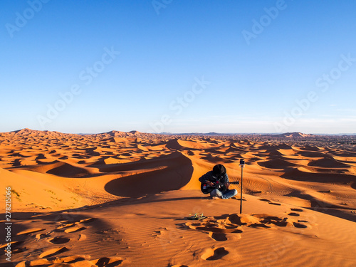 A backpacker playing guitar in Sahara Desert  Merzouga  Morocco  North Africa. Musician. Guitarist. More of the unending whipped cream dunes. Magnificent and breathtaking landscape. Natural wonder.