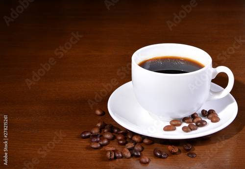 White cup of coffee and coffee beans on a wooden table. Close-up.