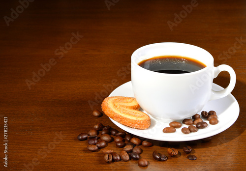 White cup of coffee and cookies on a saucer on a wooden table. Coffee beans. Dark background. Close-up.