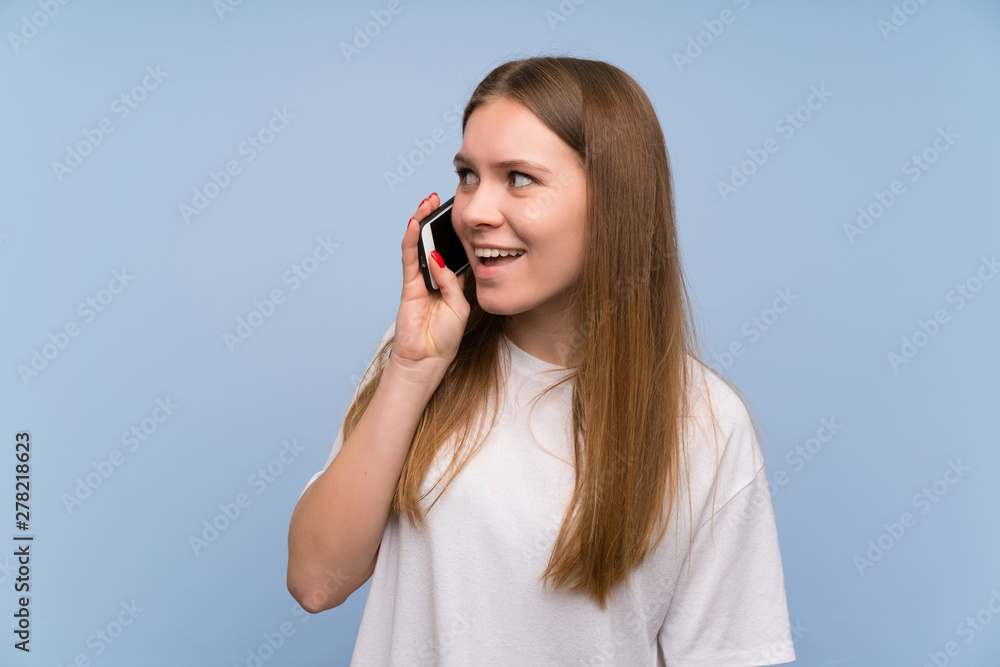 Young woman over blue wall keeping a conversation with the mobile phone Young woman over blue wall keeping a conversation with the mobile phone