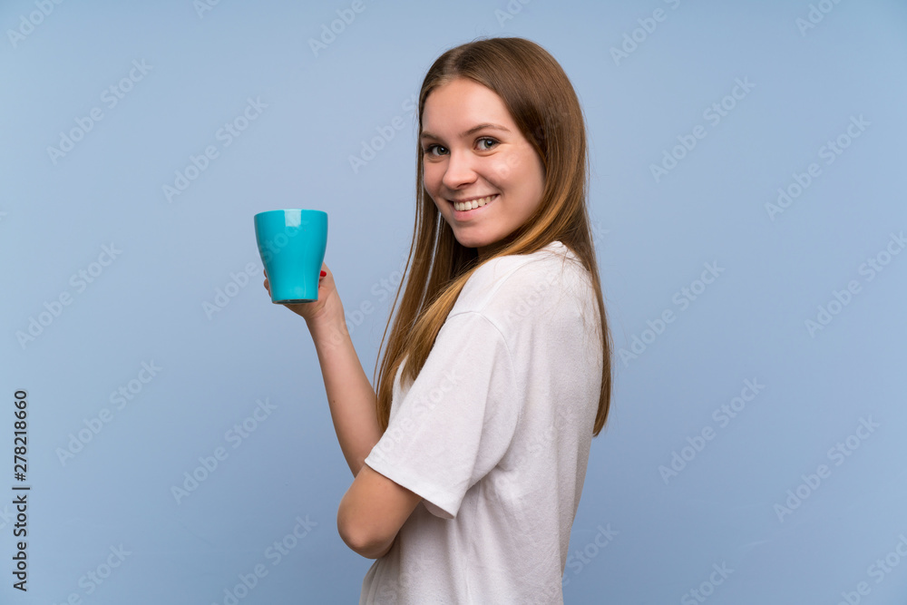 Young woman over blue wall holding a hot cup of coffee Young woman over blue wall holding a hot cup of coffee