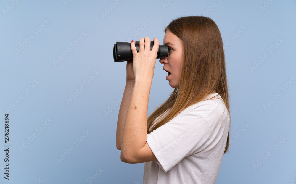 Young woman over blue wall and looking in the distance with binoculars Young woman over blue wall and looking in the distance with binoculars