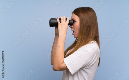 Young woman over blue wall and looking in the distance with binoculars