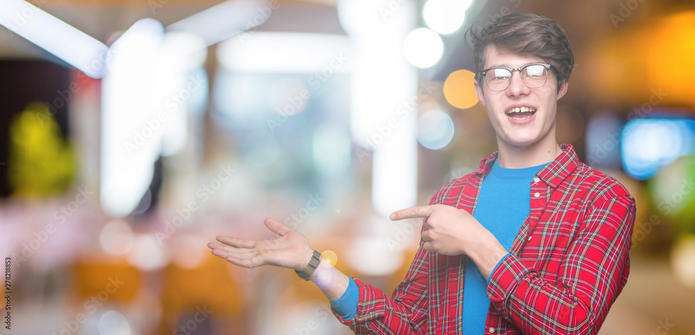 Young handsome student man wearing glasses over isolated background amazed and smiling to the camera while presenting with hand and pointing with finger. Young handsome student man wearing glasses over isolated background amazed and smiling to the camera while presenting with hand and pointing with finger.